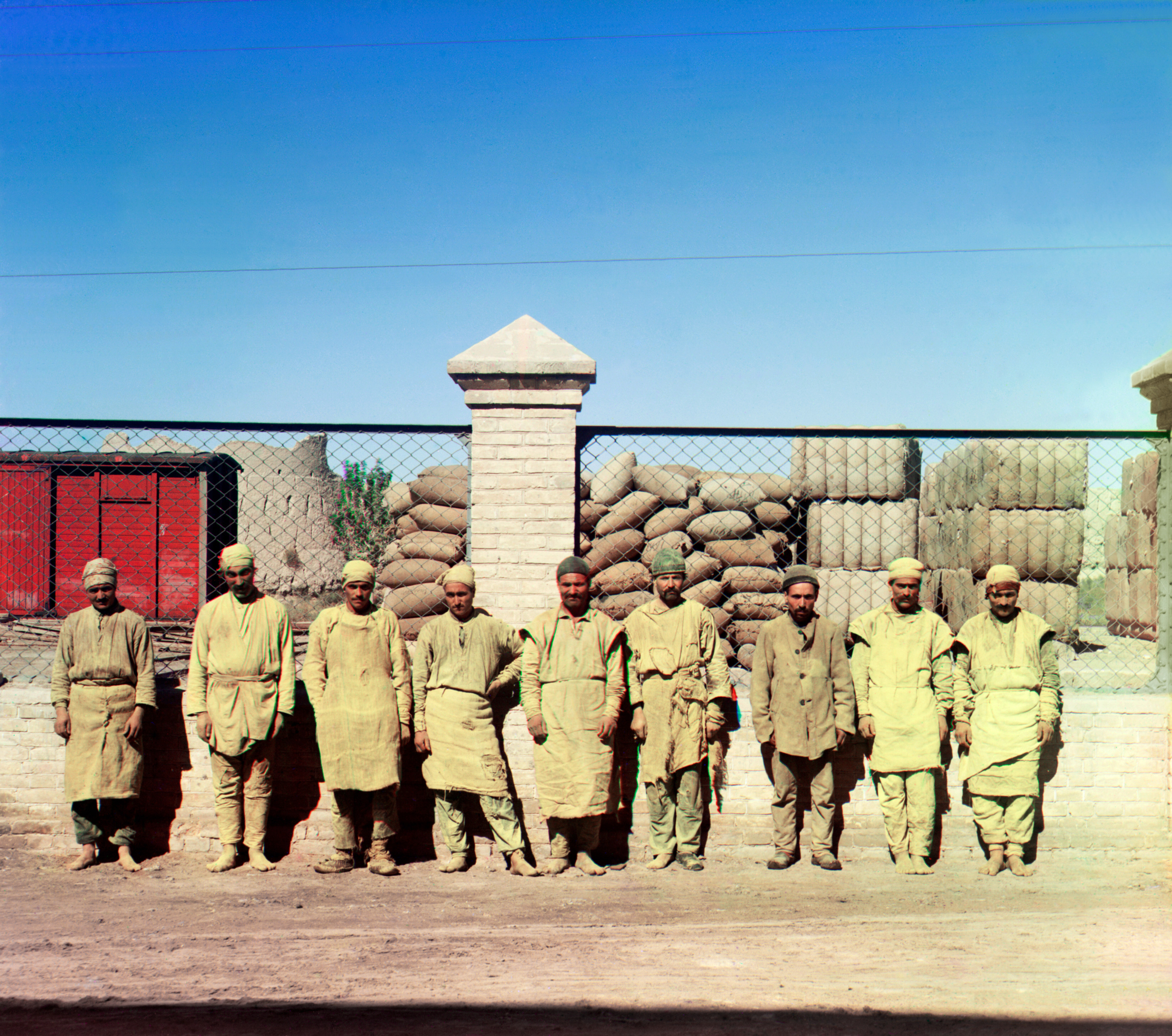 Группа рабочих стоит, позирует, перед сетчатым забором, с мешками, сложенными за забором, 1905-1915, фотограф Сергей Прокудин-Горский