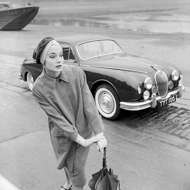 Пэт Годдард стоит у Jaguar 3.4 в черно-белом клетчатом пальто от Aquascutum и коричневой замшевой шляпе от Dolores Boutique. Vogue, ноябрь 1957 года. Фотограф Норман Паркинсон