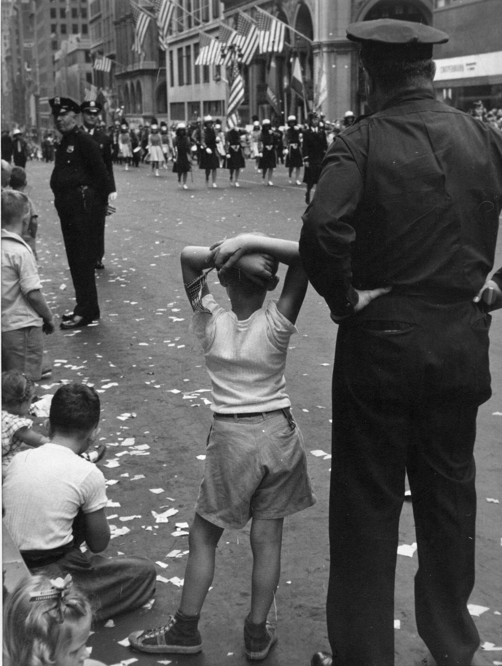 Парад, мальчик и полицейский сзади Фотограф Рут Оркин