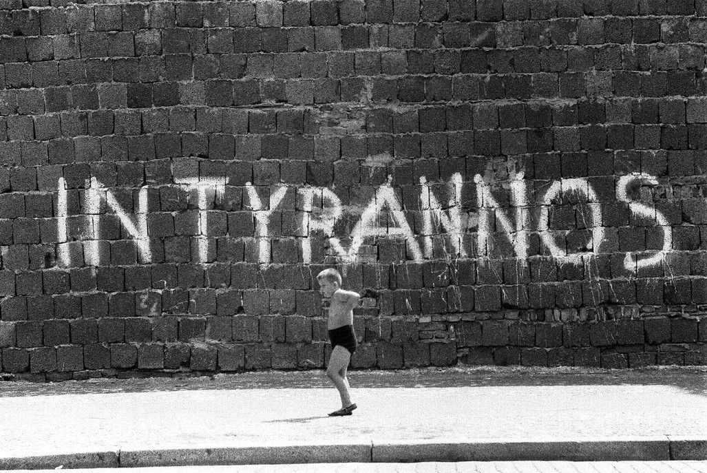 Ребенок, играющий у Берлинской стены, латинские слова In Tyrannos написаны заглавными буквами на стене, Западный Берлин, Германия, 1963 год. Фотограф Томас Хёпкер