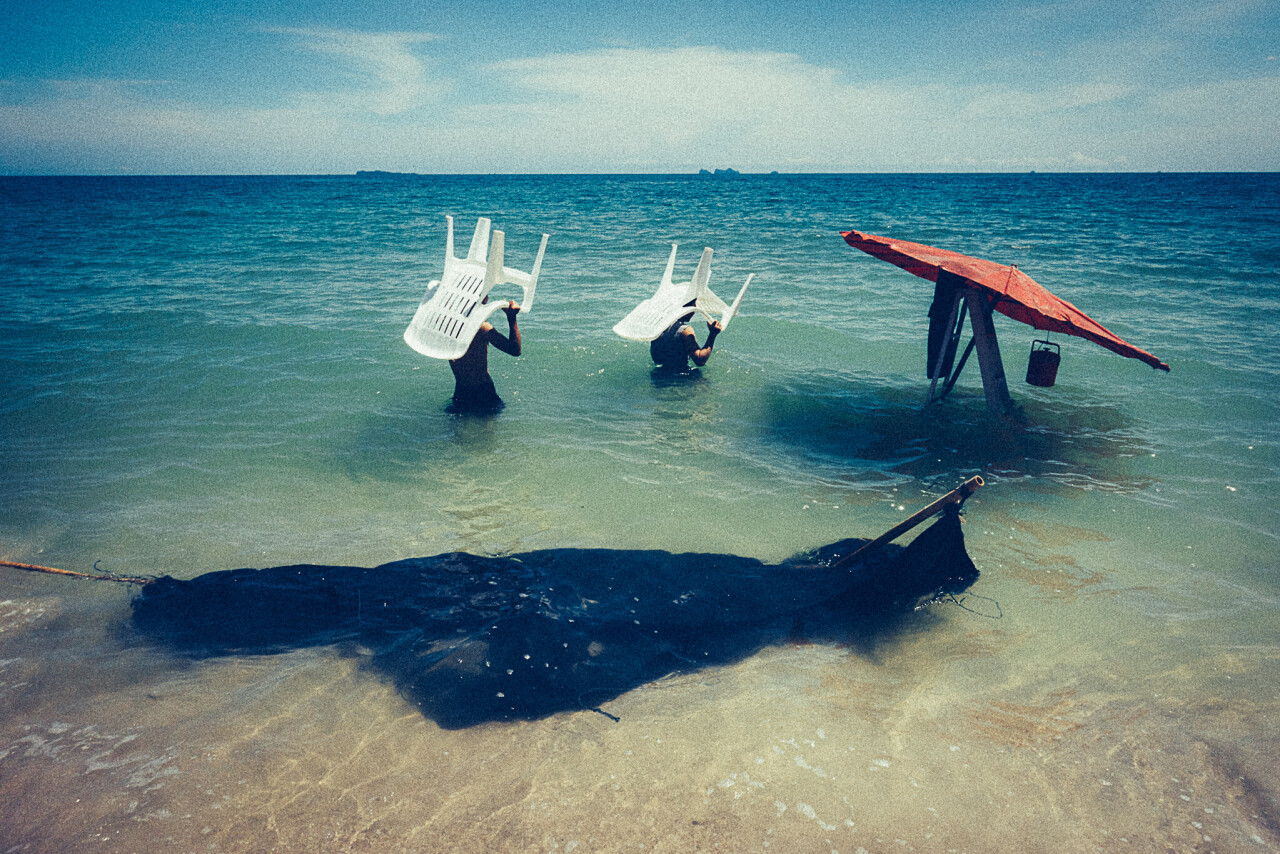 Люди со стульями уходят в море. Фотограф Ноппадол Майтричит