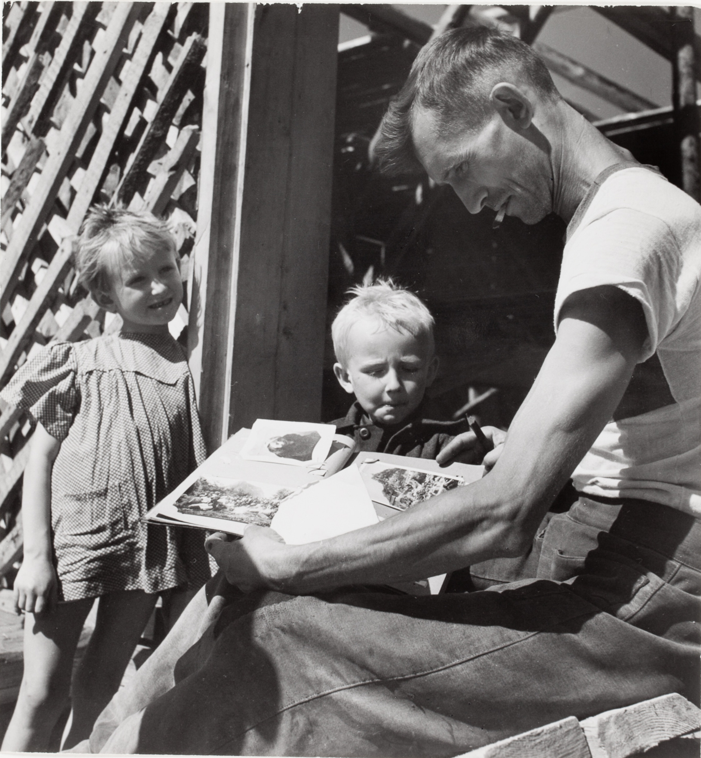 Мужчина рассматривает фотоальбом в компании детей, Сталинград, СССР, 1947 год. Фотограф Роберт Капа