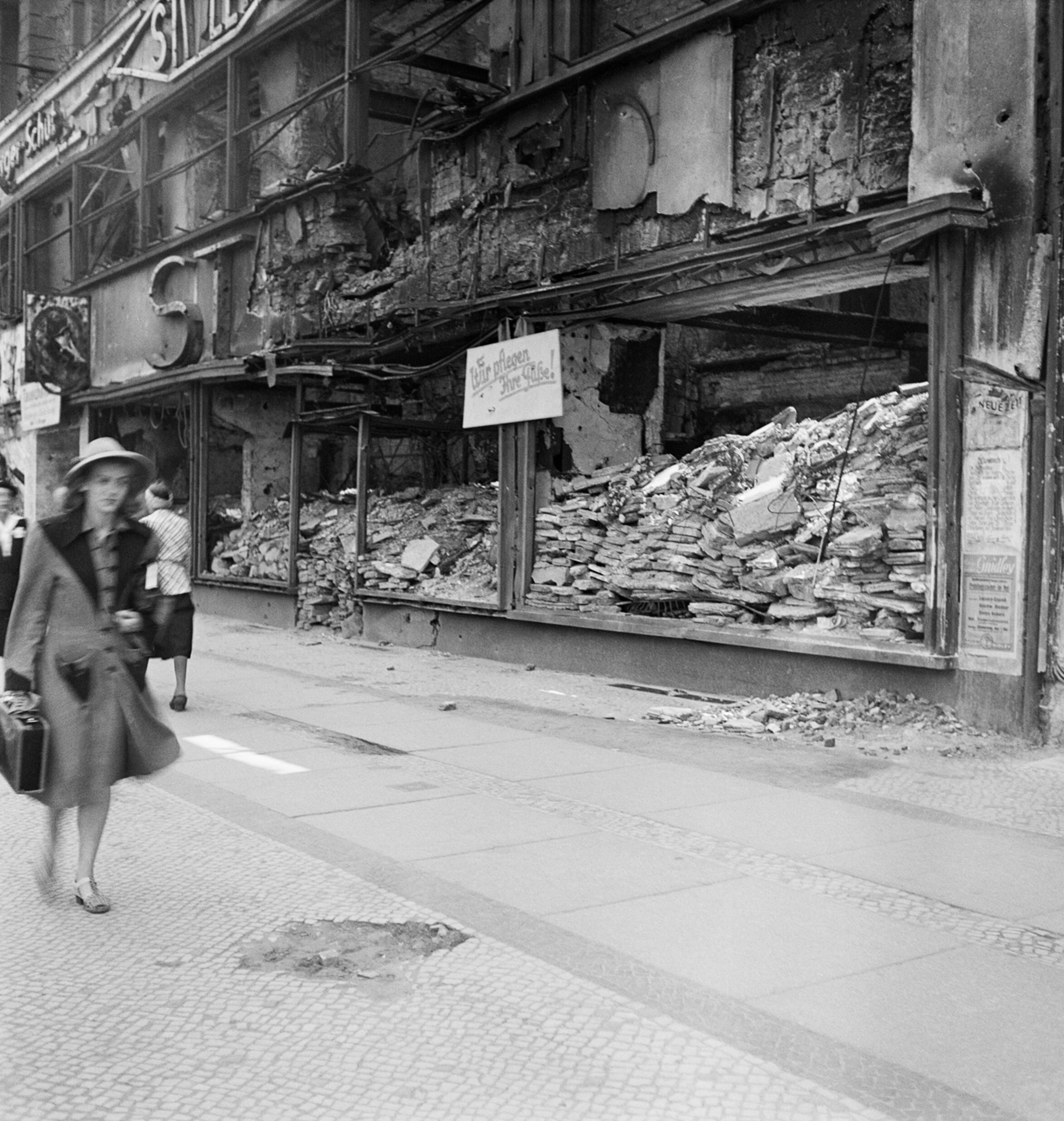 Женщина проходит мимо разрушенного обувного магазина с вывеской Мы позаботимся о ваших ногах!, Берлин, 1947 год. Фотограф Роман Вишняк