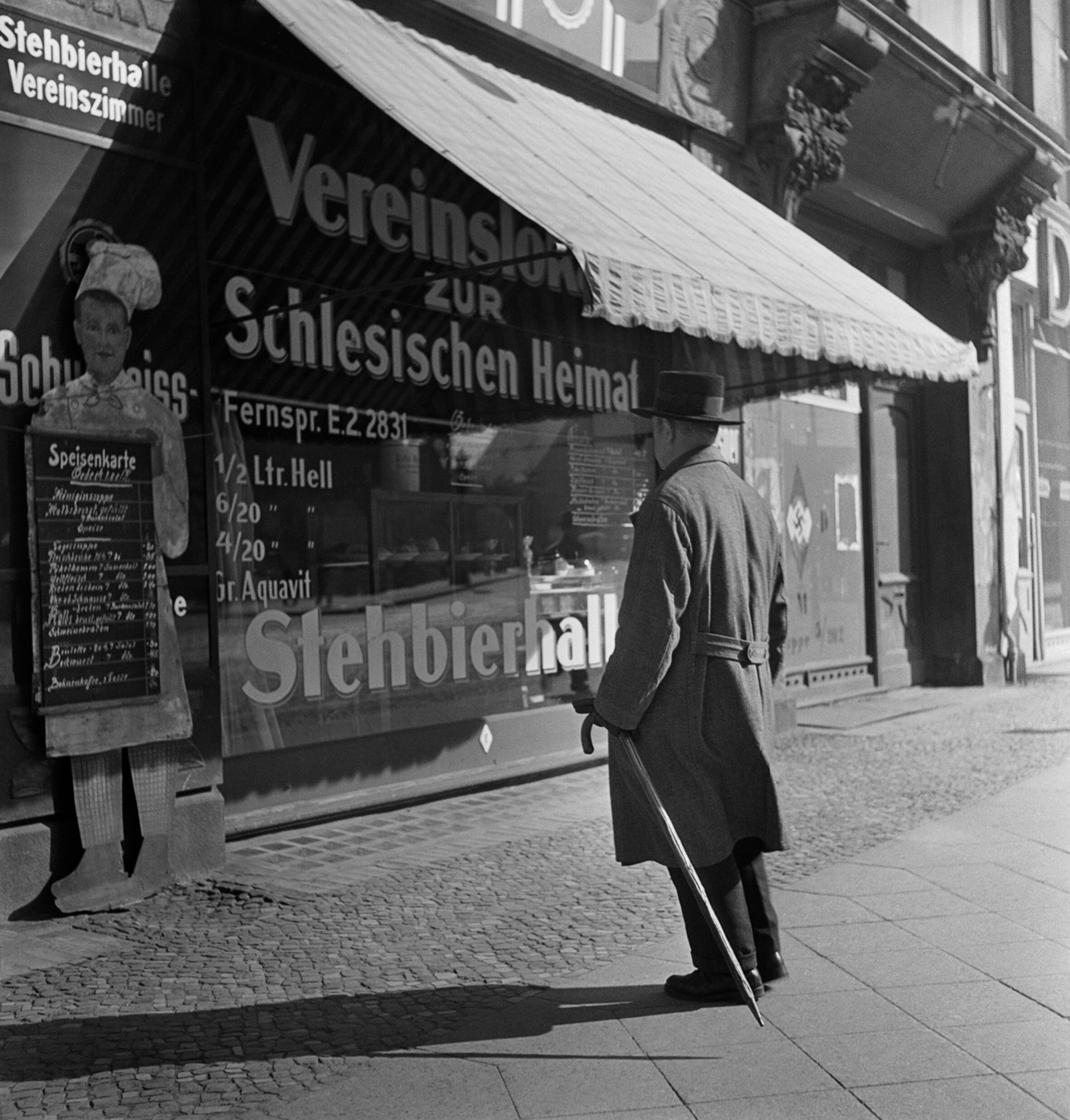 Мужчина стоит перед клубом и пабом Силезской Родины, на стене справа нарисована свастика, Берлин, середина 1930-х годов. Фотограф Роман Вишняк
