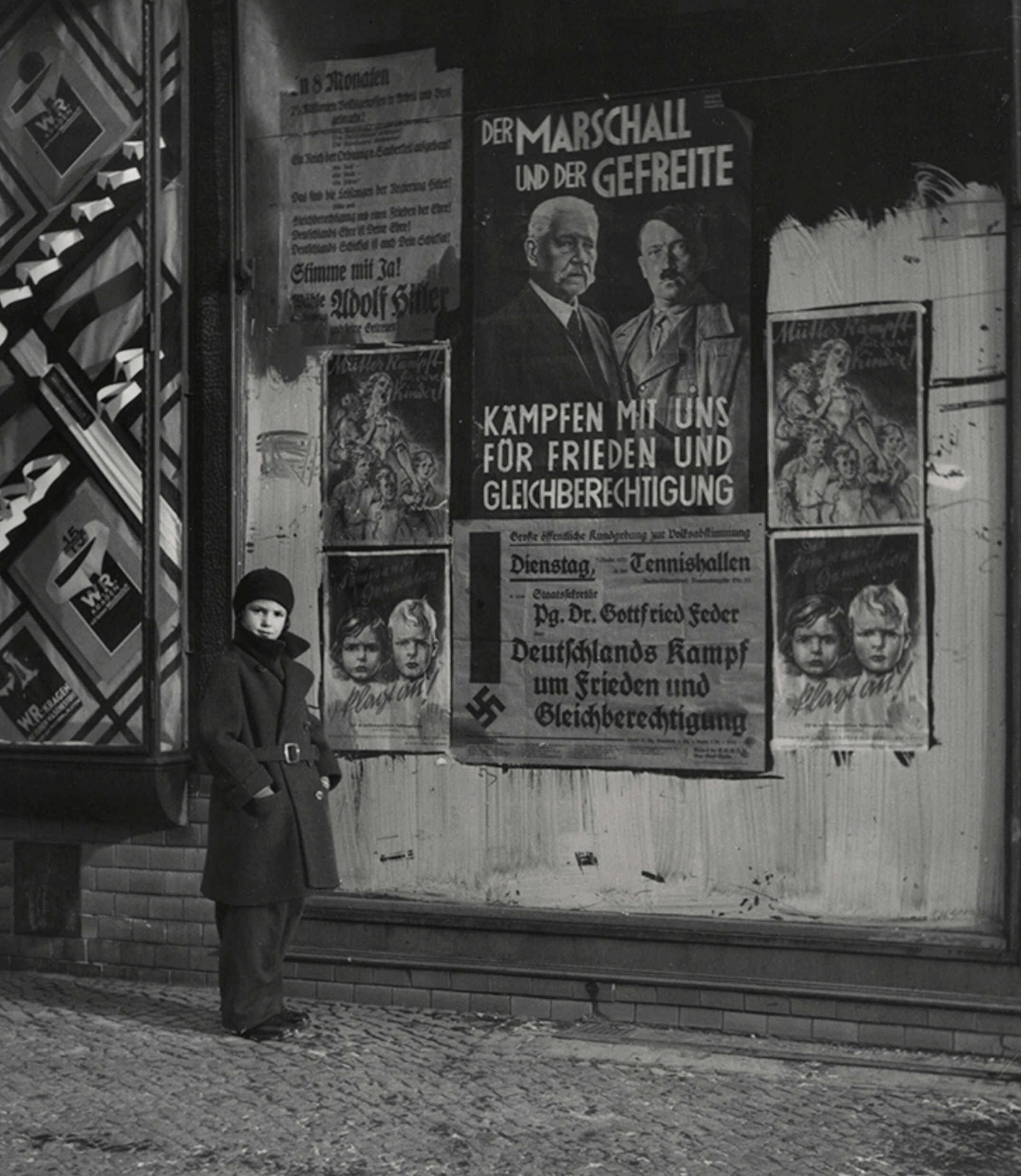 Дочь Вишняка Мара позирует перед предвыборным плакатом Гинденбурга и Гитлера с надписью Маршал и капрал сражайтесь с нами за мир и равные права, Вильмерсдорф, Берлин, 1933 г. Фотограф Роман Вишняк